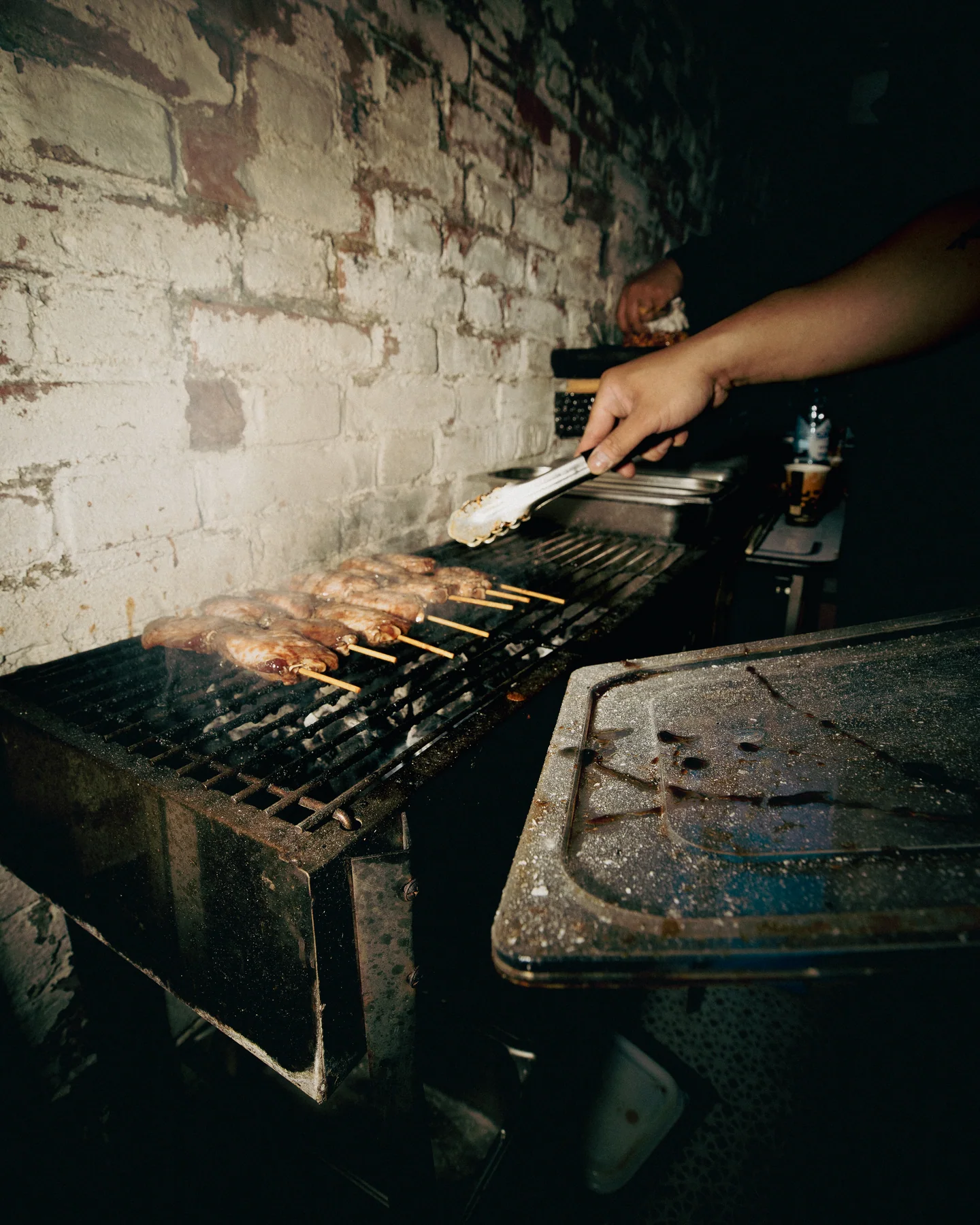 Barbecue skewers cooking on a grill beside a brick wall at TAYO Community BBQ